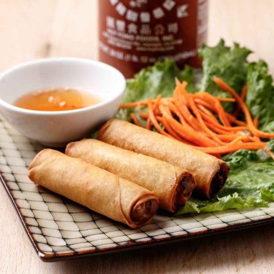 Three crispy Vietnamese egg rolls on a plate with lettuce, shredded carrots, and dipping sauce.